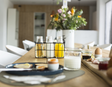 Gedekte ontbijttafel met vers sap, een eitje, glas melk en een houten plank met smeersels. 