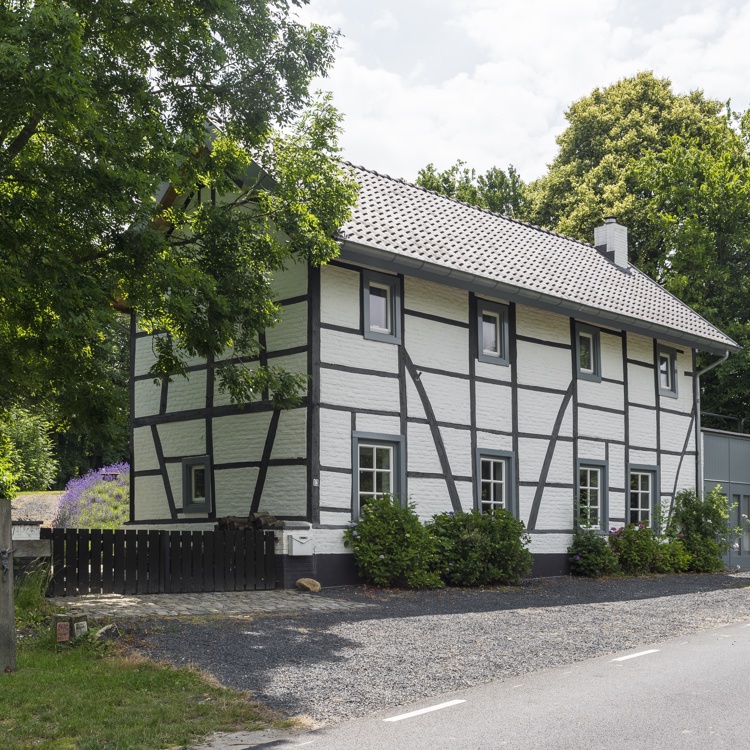 Vakwerkhuisje langs de weg met veel groen eromheen 