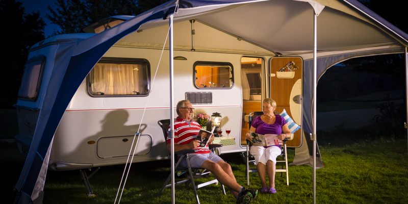 Echtpaar zit in de avond op twee stoelen voor de caravan. 