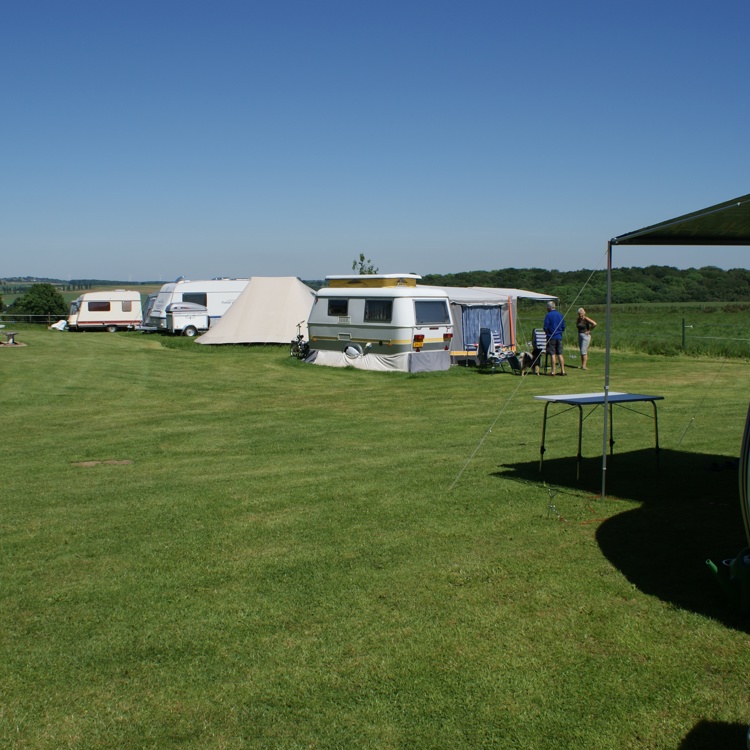 Vlakke weide met gras en enkele caravans. 