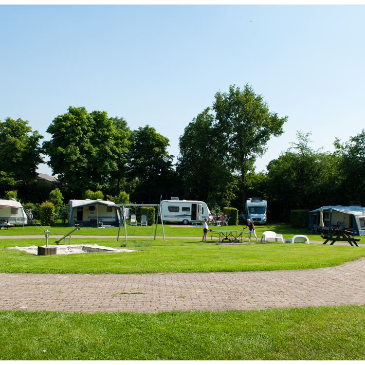 Vlakke weide met gras en enkele caravans. 