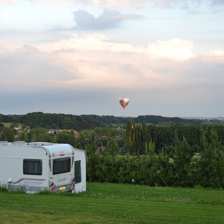 Caravan op de voorgrond met daarachter een weids uitzicht en een luchtballon in de lucht. 