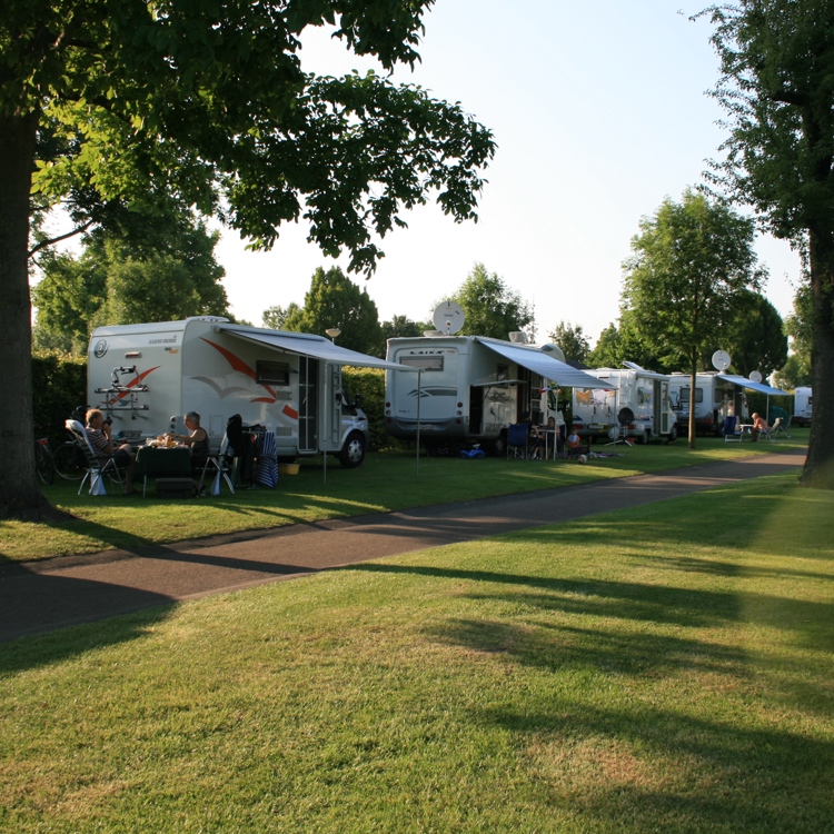 Vlakke camperplaats met diverse campers naast elkaar en mensen ervoor. 