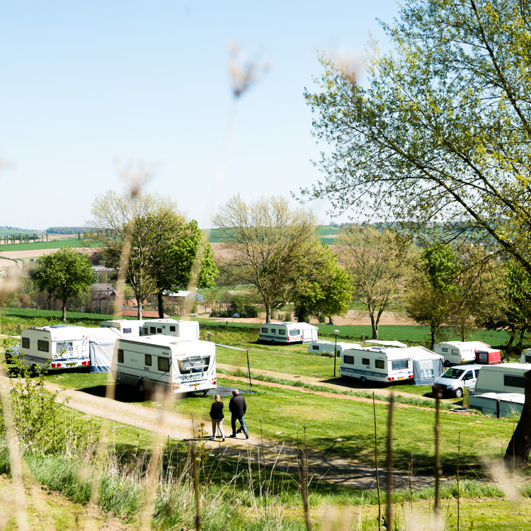 Camping met grasveld, enkele caravans en in de verte de glooiende heuvels. 