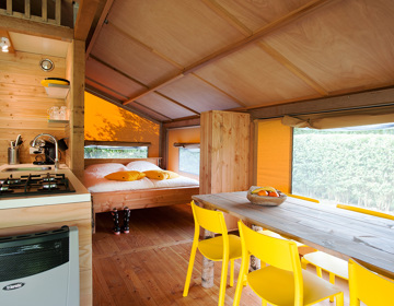 Interieur van een luxe tent met tweepersoons bed, keukentje en eettafel. 