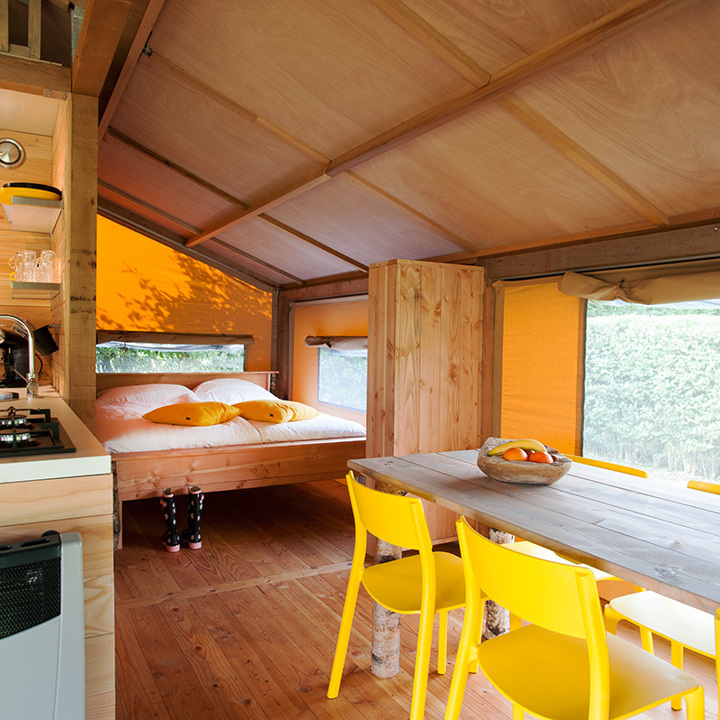 Interieur van een luxe tent met tweepersoons bed, keukentje en eettafel. 