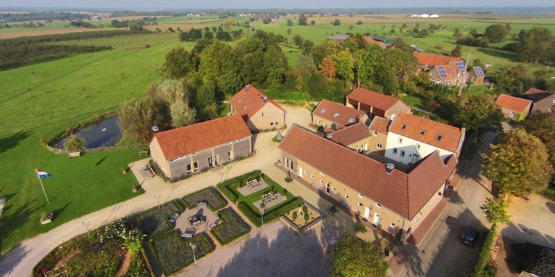 Bovenaanzicht van een grote boerderij met tuin en land eromheen. 