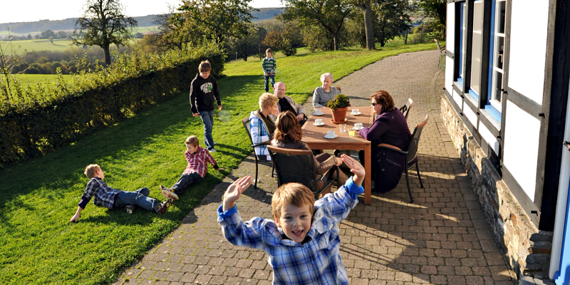 Kinderen spelen in het gras terwijl ouders gezellig bijkletsen aan tafel