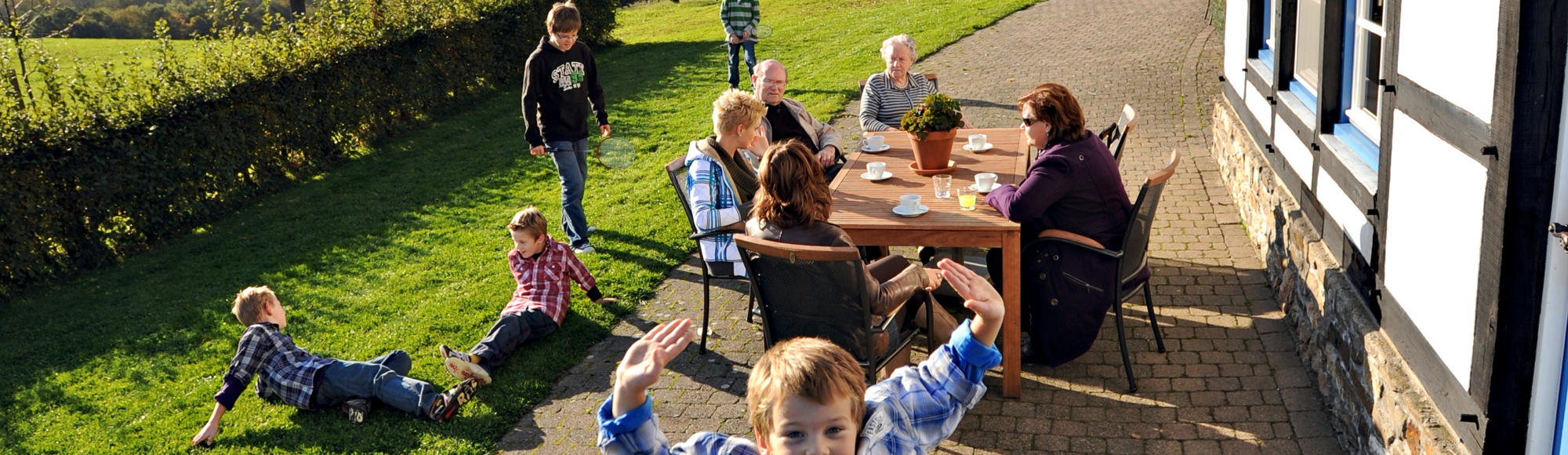 Kinderen spelen in het gras terwijl ouders gezellig bijkletsen aan tafel