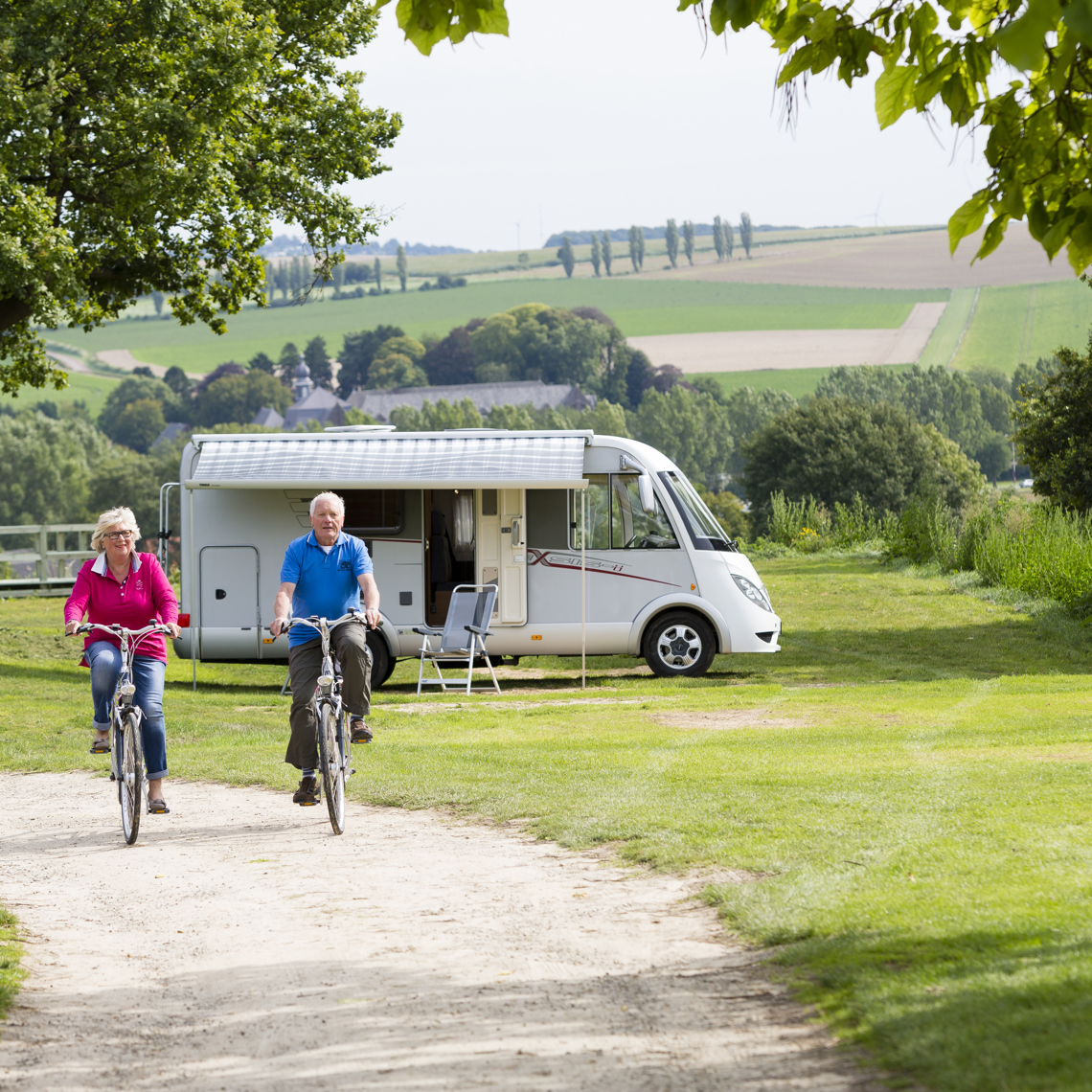 Echtpaar fietst over de camping met op de achtergrond een camper. 