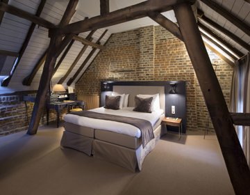 Sfeervolle hotelkamer onder houten balken met een luxe opgemaakt bed. 