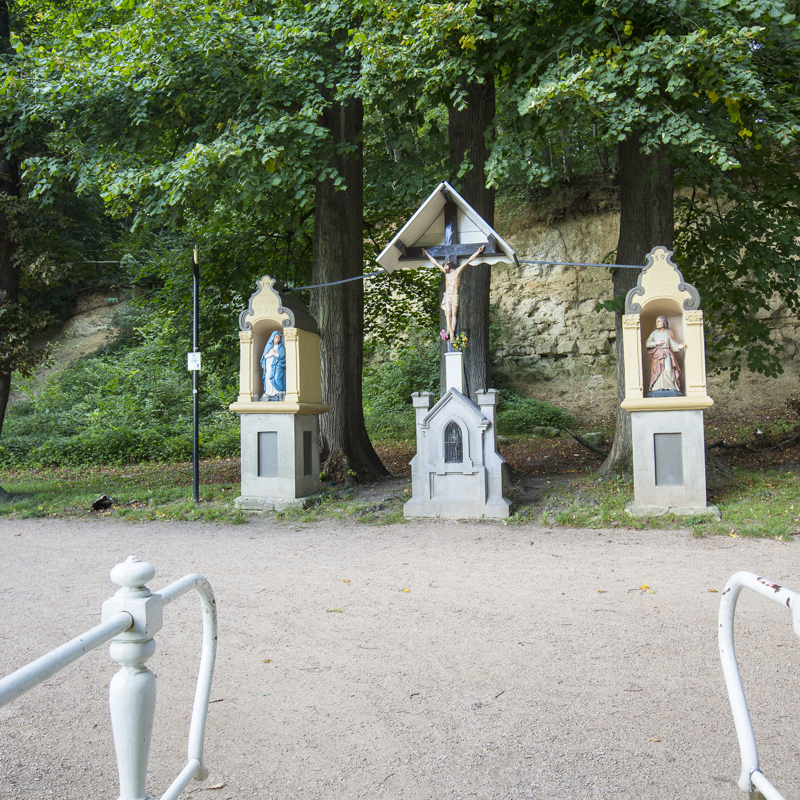 3 bijbelse beelden op sokkels voor bomen gezien vanaf een bruggetje