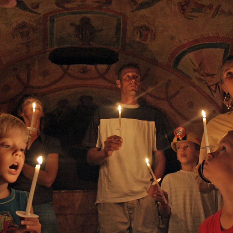 Mensen en kinderen die ieder een kaars vasthouden in de Romeinse Katakomben van Valkenburg