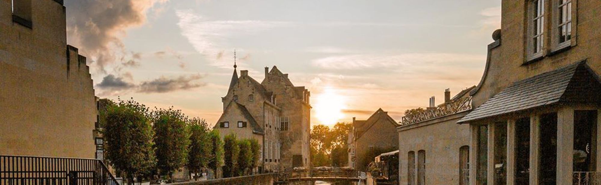 Beeld van Valkenburg met ondergaande zon vanaf met bloemen versierde brug richting Geulpoort