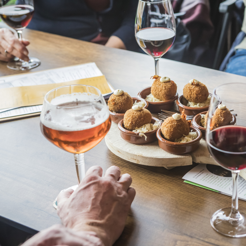 Close up van bitterballen met daarop een toefje van een wit sausje te midden van glazen rode wijn en speciaal bier