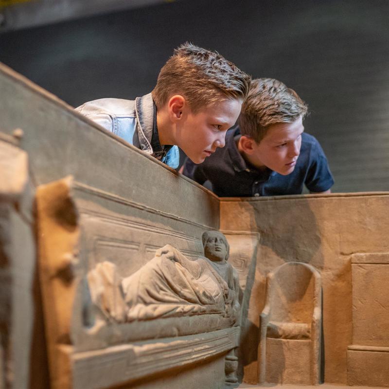 Twee kinderen bestuderen de binnenkant van de Sarcofaag van Simpelveld in het Romeins Museum Heerlen
