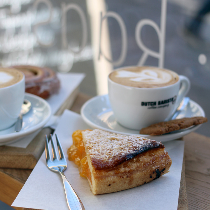 Close up van houten plankje met daarop een stuk abrikozenvlaai en een cappuccino