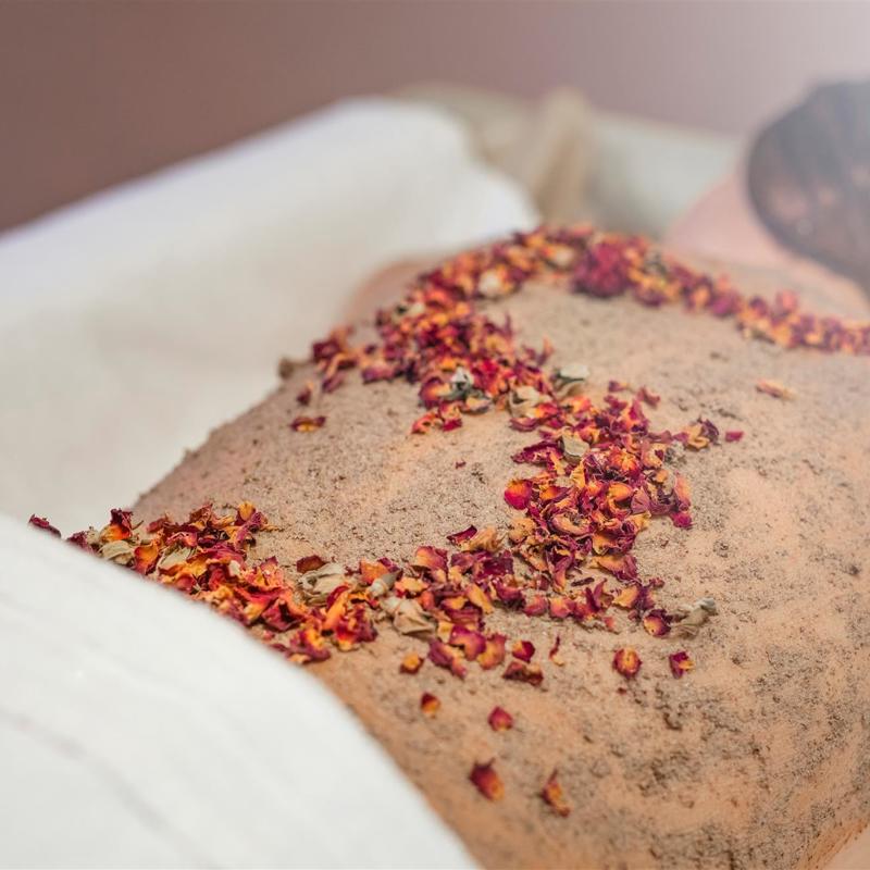 Blote rug van vrouw op behandeltafel met daarop scrub en rood oranje blaadjes