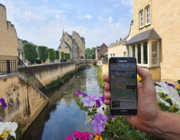 Hand die smartphone vasthoudt met plattegrond op scherm in beeld van Geul door centrum Valkenburg