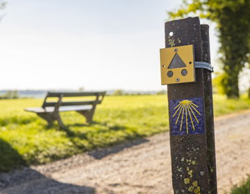 Close up van bewegwijzeringspaaltje naast onverharde veldweg en rustbankje