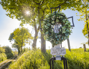 Wegkruis met krans van klimop naast veldweg en bomen