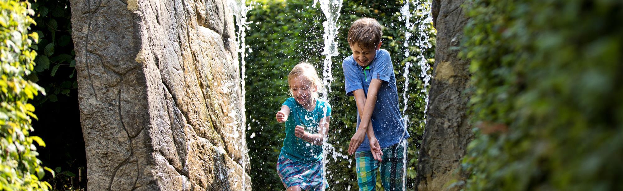 Kinderen proberen niet nat te worden van de fonteinen in het labyrint van het Drielandenpunt in Vaals
