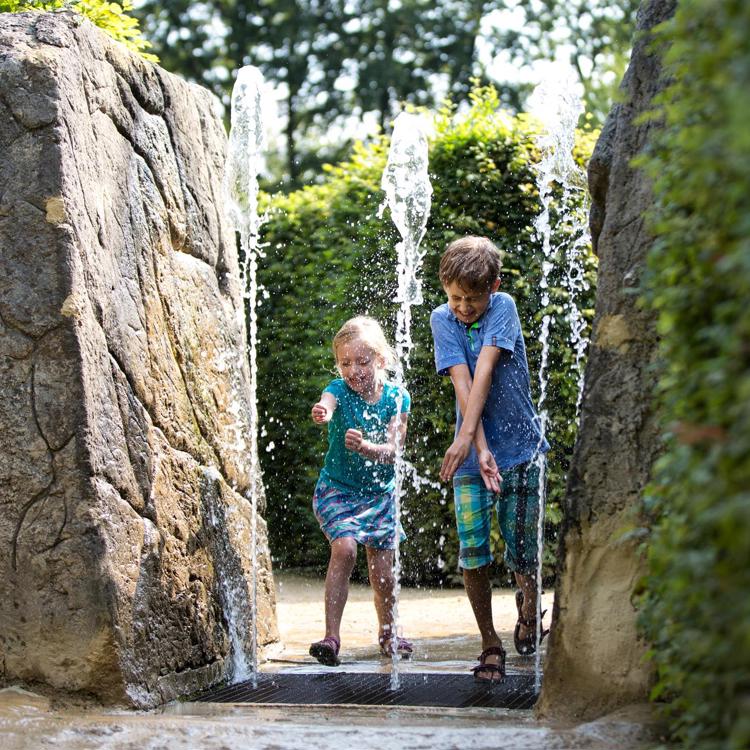 Kinderen proberen niet nat te worden van de fonteinen in het labyrint van het Drielandenpunt in Vaals
