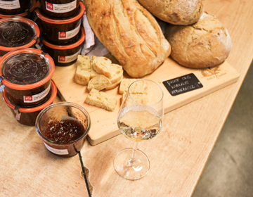 Close up van houten plank met verschillende broden naast glas witte wijn en weckpotjes met jam