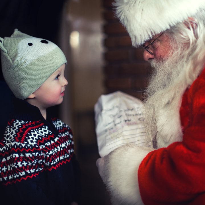 Jongetje met Noorse trui en dierenmuts kijkt kerstman in de ogen