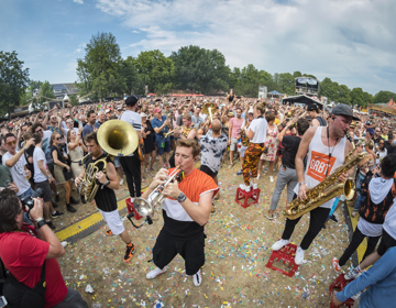 Jonge mannen met blaasinstrumenten staande op bierkratjes in het midden van bezoekers van festival in Parkstad