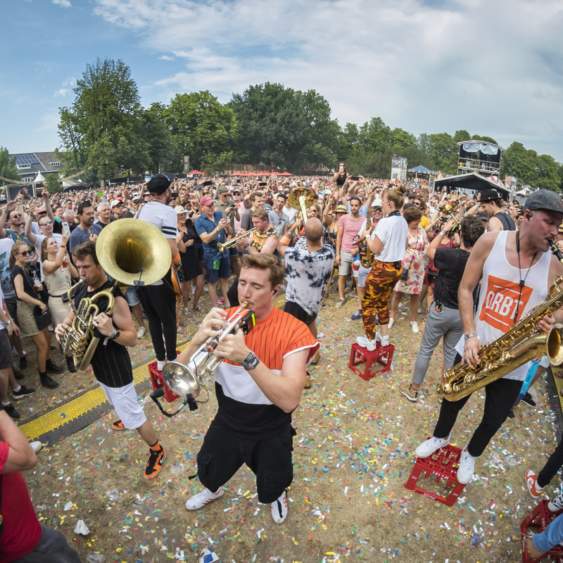 Jonge mannen met blaasinstrumenten staande op bierkratjes in het midden van bezoekers van festival in Parkstad