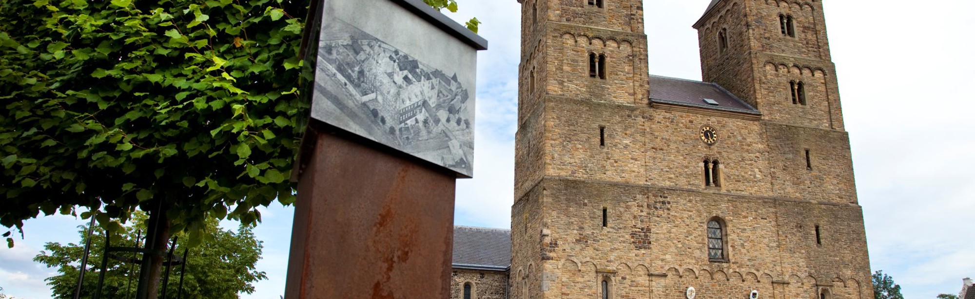 Amelberga basiliek in Susteren - voorkant gefotografeerd vanaf het plein met een historisch weergave op infopaal