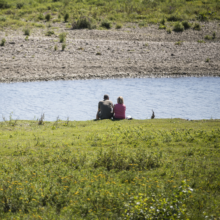 twee mensen zittend aan de waterkant in het RivierPark Maasvallei