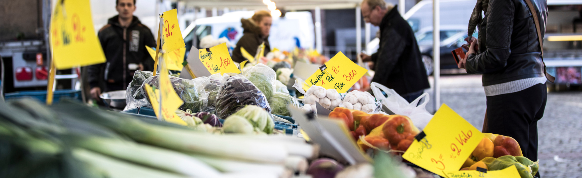 Mensen staan aan een groentekraam op de markt