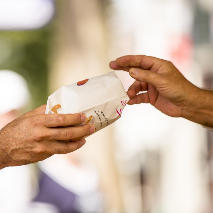 Personen geven elkaar een papierenzakje op de markt. Alleen hand en arm te zien