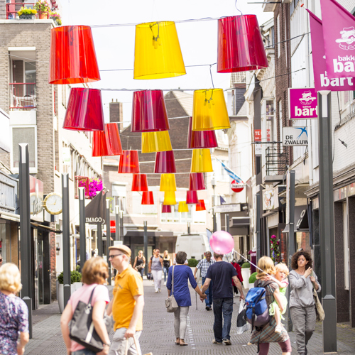 Mensen lopen door de met rode en gele lampen versierde winkelstraten van Heerlen