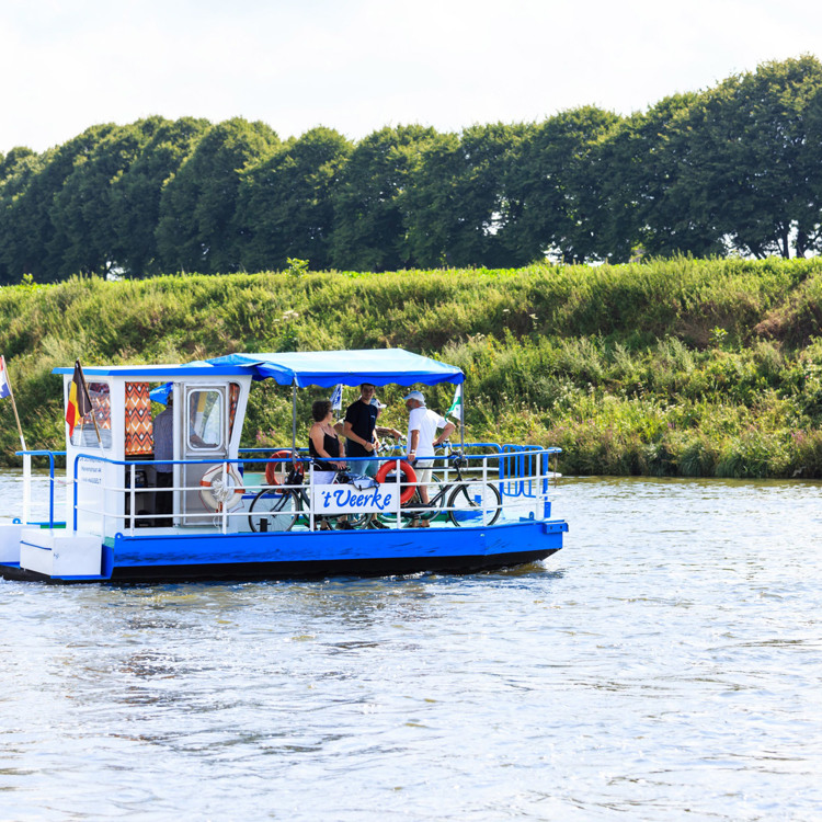 Het veerpontje met fietsers steekt de Maas over van Nederland naar België