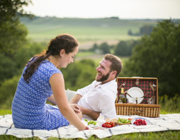 Man en vrouw genieten op weide van een picknick met achterliggend heuvellandschap