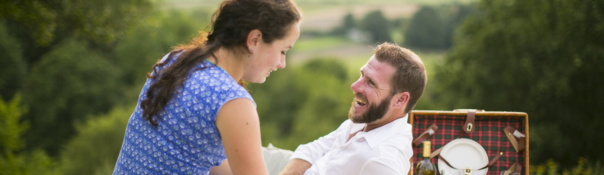 Man en vrouw genieten op weide van een picknick met achterliggend heuvellandschap