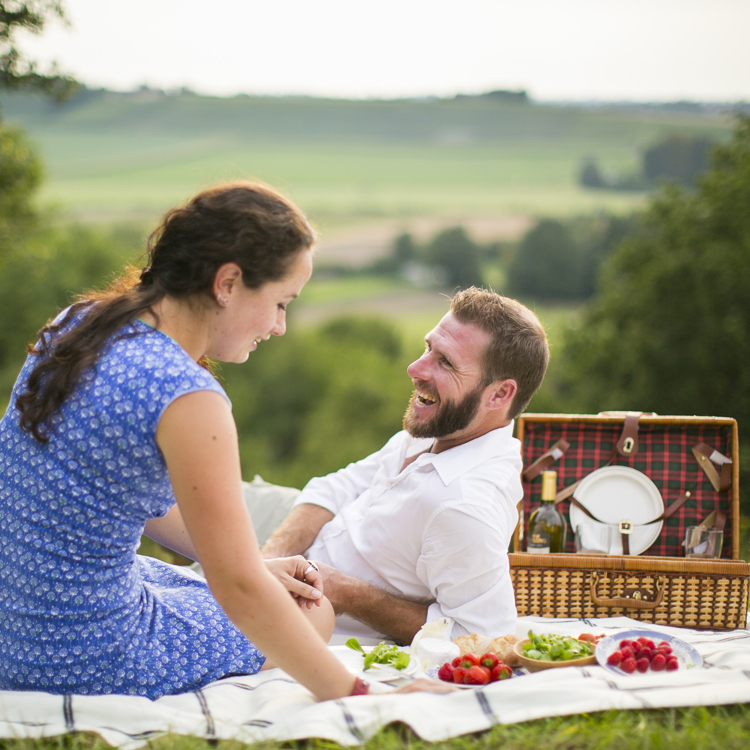 Man en vrouw genieten op weide van een picknick met achterliggend heuvellandschap