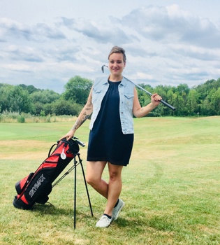 Vrouw poseert naast golftas met golfclub in haar nek op golfbaan
