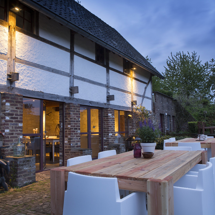 Groot terras met witte stoelen en houten tafels bij schemering.