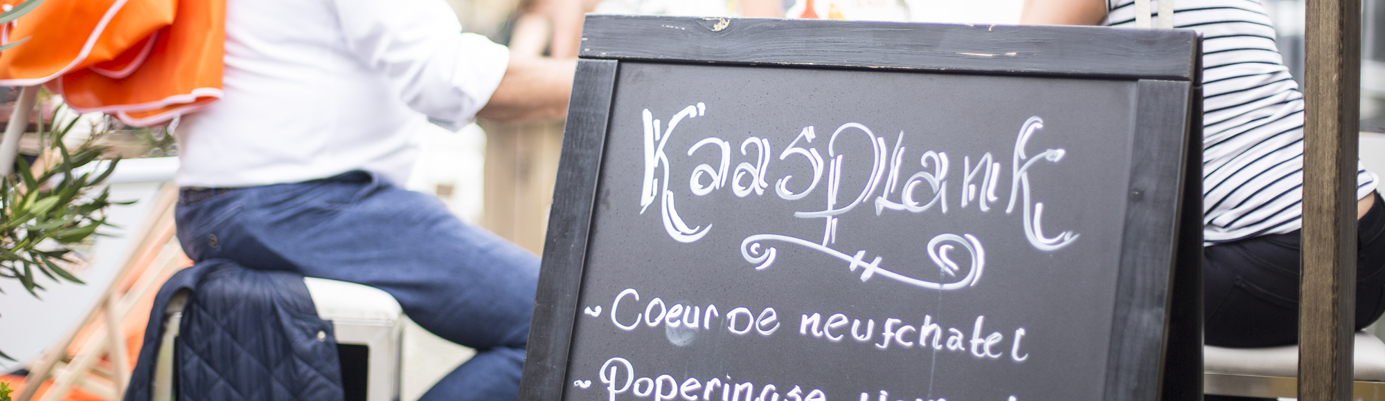 Twee vrouwen en een man zitten aan een hoge tafel achter een bord met het kaasplank menu