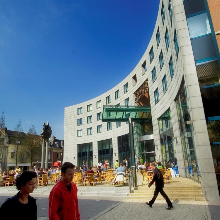 Mensen zitten op het terras en lopen langs de ingang van het Corio Center in Heerlen