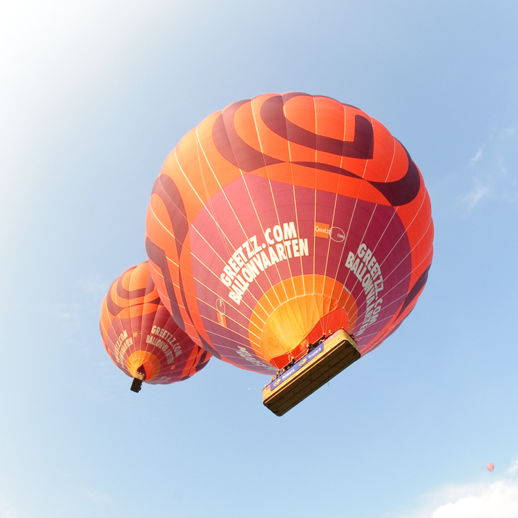 2 grote oranjerode luchtballonnen in lichtblauwe lucht van onderaf gefotografeerd