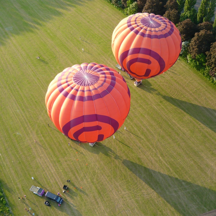 bovenaanzicht van twee oranje/paarse gevulde luchtballonnen op een grasveld