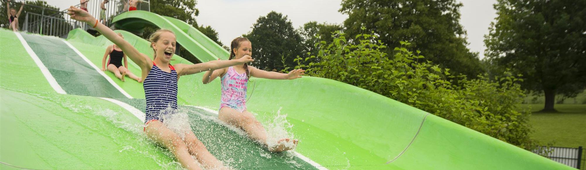 Kinderen glijden van glijbaan in buitenbad van Mosaqua