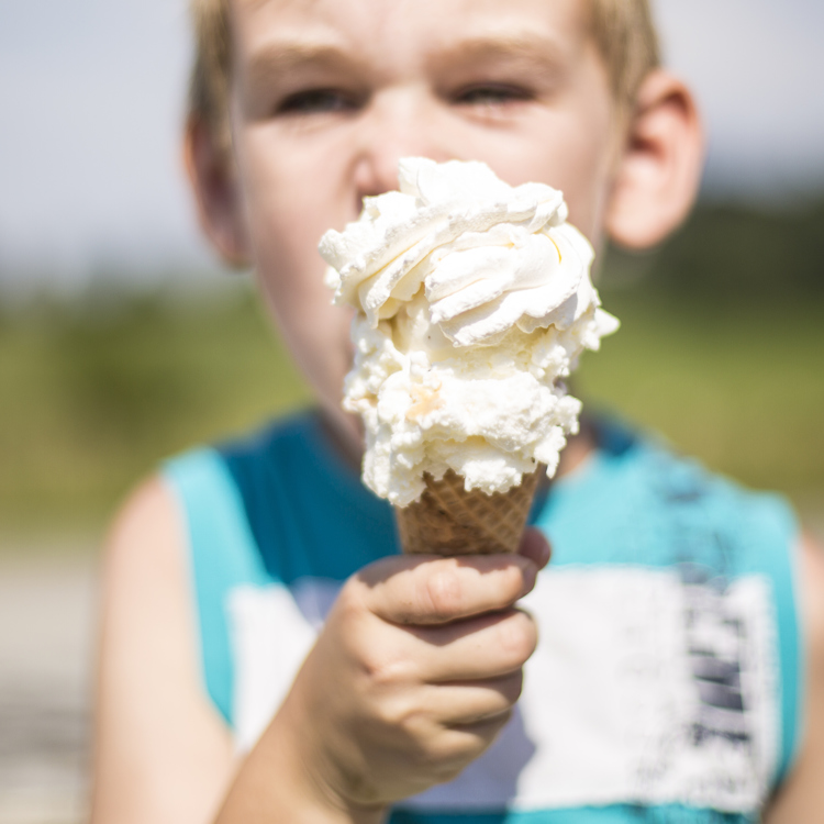 Een jongetje eet een heel groot ijsje met extra slagroom op een hoorntje