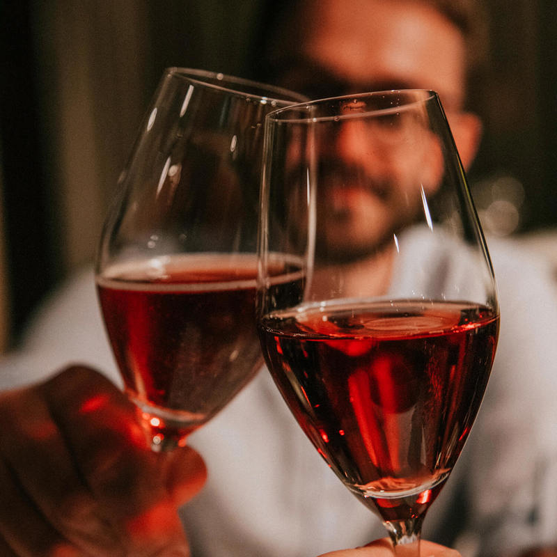 Een man proost met iemand met twee rose wijnen