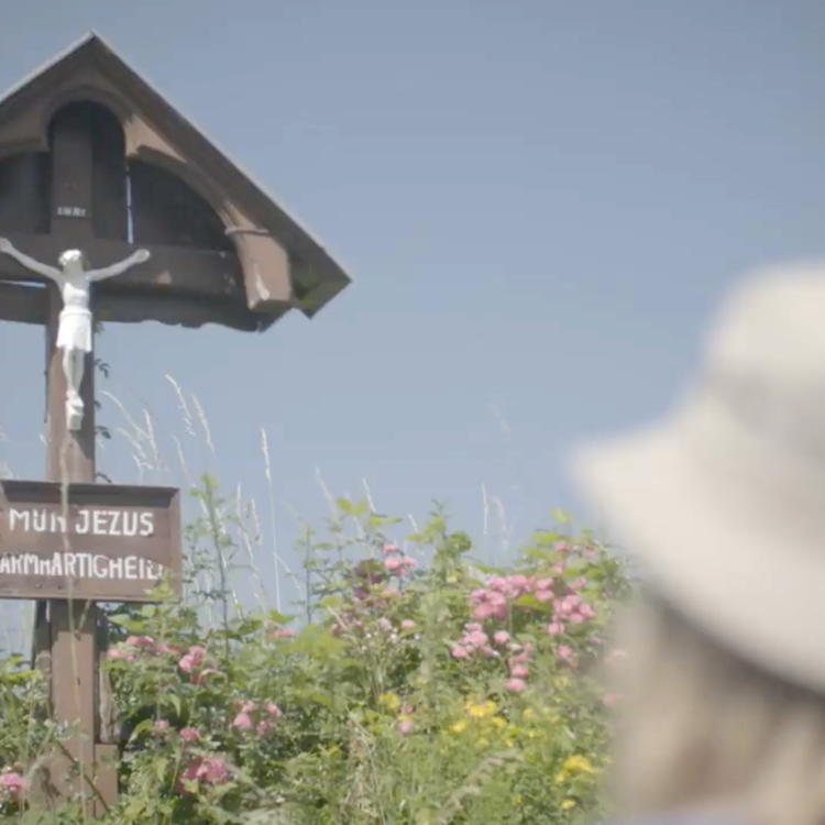 Wandelaarster voor wegkruis Mijn Jezus Barmhachtigheid met bloemen Mijn Pelgrimspad